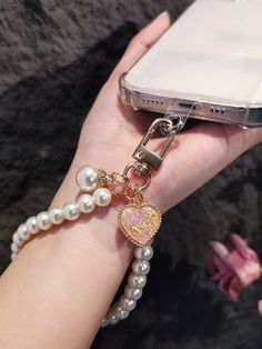 a person holding a cell phone with pearls on it and a heart charm attached to the wrist