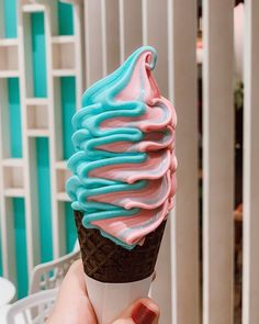 a person is holding up an ice cream cone with blue and pink icing