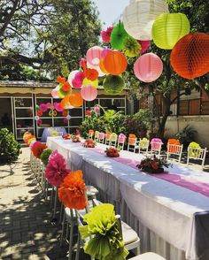 a long table with paper lanterns hanging from it's ceiling and flowers on the tables
