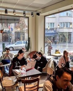 people sitting at tables in a restaurant with large windows looking out on the city street