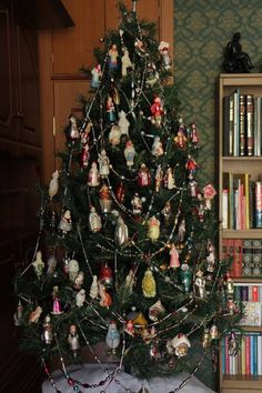a christmas tree with ornaments on it in front of a bookshelf filled with books