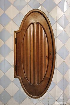 an oval wooden door in the middle of a tiled wall with blue and white tiles