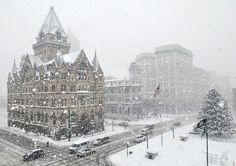 a snowy day in the city with traffic and buildings