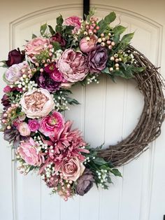 a wreath with pink and purple flowers hanging from the front door, on a white door