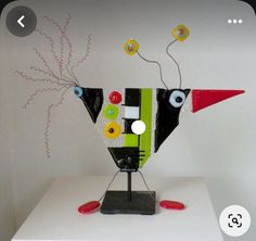 a sculpture made out of paper and buttons on a white surface with an image of a bird in the background