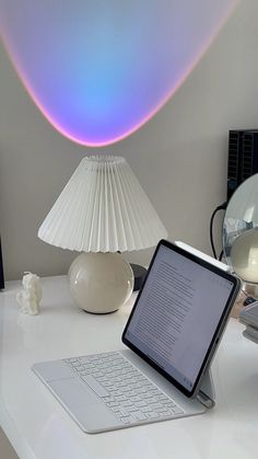 an open laptop computer sitting on top of a white desk next to a lamp and mirror