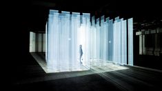 a person standing in an empty room with sheer curtains on the wall and light coming through them