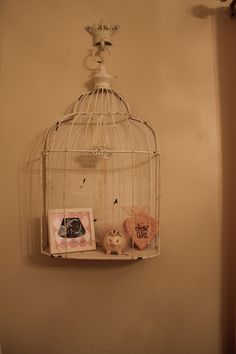a white birdcage hanging on the wall next to a shelf with pictures and other items
