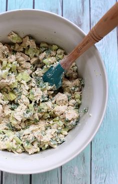 a white bowl filled with chicken salad on top of a blue wooden table next to a green spatula