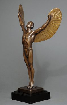 a bronze statue with wings on top of a wooden base
