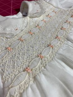 an embroidered white dress with pink flowers on the collar and sleeves, sitting on a table