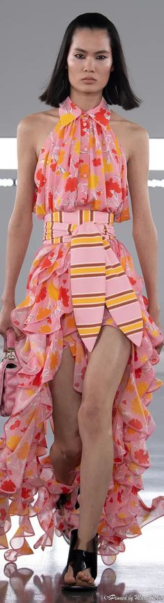 a woman is walking down the runway in a pink and yellow dress with ruffles