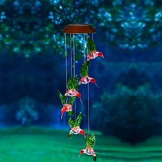 a wind chime hanging from a tree filled with green leaves and red hummings