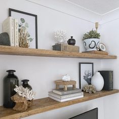 two wooden shelves with books and vases on them in a white walled room area