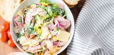a salad with ham, cheese and lettuce in a bowl next to bread