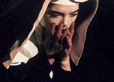 a nun holding her hands to her face while wearing a black and white outfit with the cross on it
