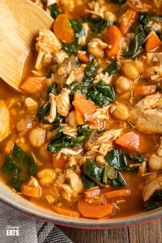 a wooden spoon in a bowl filled with chicken, beans and spinach soup on top of a table