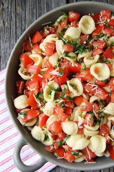 a pan filled with pasta and tomatoes on top of a wooden table next to a striped napkin