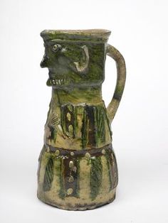 Green glazed jug with brown, green and cream stripes, top decorated with a man's bearded face,body of the jug show the man's arms & hands, hands are clenched together. Kingston-type ware like this, are usually highly decorated conical jugs with anthropomorphic motifs. Jugs with faces were very popular and most of the potteries around London made them,often show a man pulling his own beard.  perhaps it's a medieval joke or caricature that has been forgotten over time.  1301 AD - 1400 AD 14th Century, Prehistoric, Medieval, High Quality Art Prints, Medieval Life, Face Jugs, The Potter's Hand, Museum