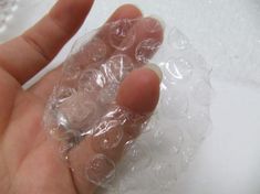 a hand holding some clear plastic on top of a white surface with bubbles in it