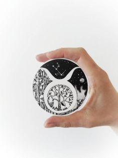 a hand holding a black and white clock with trees on it in front of a white background