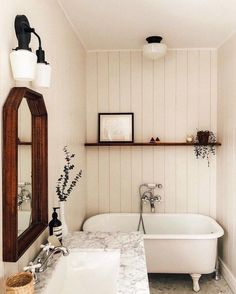 a white bath tub sitting next to a sink under a bathroom mirror on top of a wooden shelf