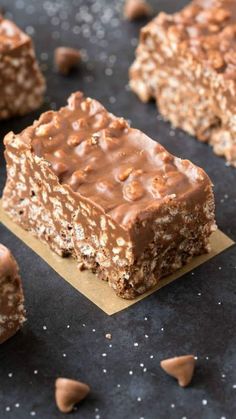 two pieces of chocolate peanut butter granola bars on top of a black surface with scattered nuts