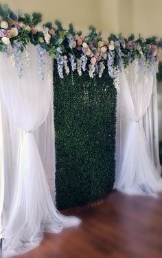 an arrangement of flowers and greenery is displayed on the side of a wall with sheer curtains