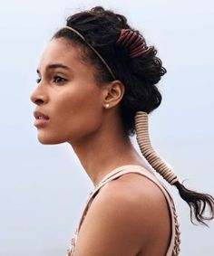 a woman with braids in her hair looks off to the side while standing against a blue sky