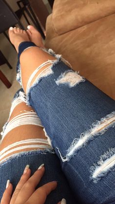 a woman's legs with ripped jeans and white nail polishes on her feet