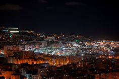 the city lights shine brightly at night in this view from atop a hill, with buildings lit up