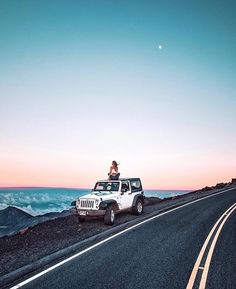 a person sitting on top of a white jeep driving down a road next to the ocean