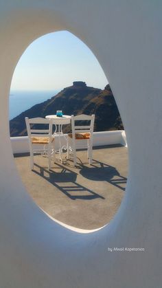two white chairs sitting at a table in front of a window with a view of the ocean