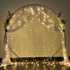 an arch decorated with lights and flowers on top of a wooden floor in front of a wall