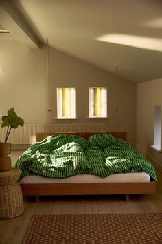 a bed with green sheets and pillows in a room next to two windows on the wall