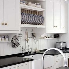 a kitchen with white cabinets and black counter tops is pictured in this image, there are plates stacked on the shelves above the sink