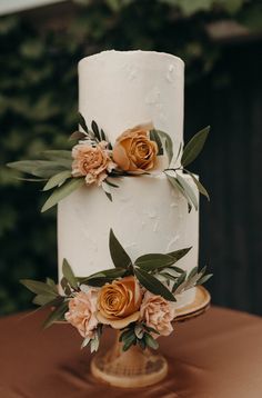 a three tiered white cake with orange flowers on top and greenery around the edges