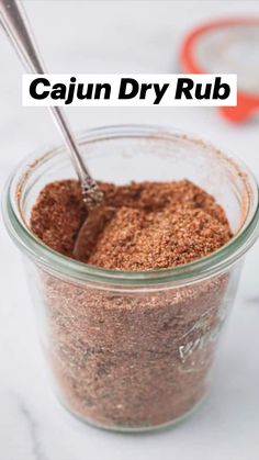 a jar filled with spices on top of a white counter next to a red measuring spoon