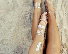 two women with tattoos on their legs laying in the sand