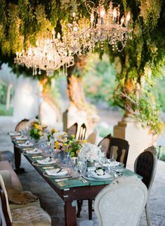an outdoor dining table with chandelier hanging from it's centerpieces