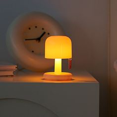 a yellow lamp sitting on top of a white table next to a clock and books