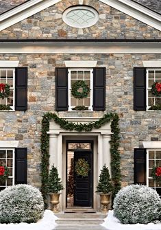the front entrance to a large stone house decorated with christmas wreaths and potted plants