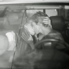 black and white photograph of two people in a car, one kissing the other's head