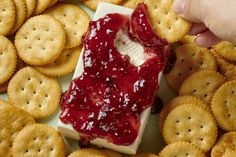 crackers and cheese with strawberry jam spread on them are being held by a hand