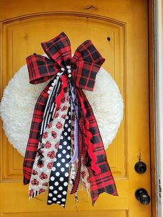 a red and black plaid bow hangs on a yellow front door with white fur ball