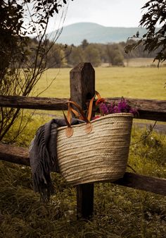 a woven basket with flowers in it sitting on a wooden fence