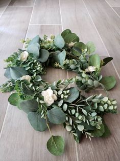 a wreath made out of eucalyptus leaves and white flowers on a wooden floor with tile
