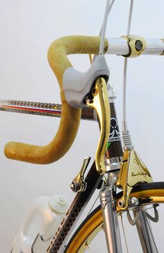 a close up of a bike handlebars on a white and yellow bicycle with gold accents