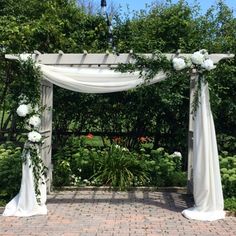 an outdoor wedding ceremony setup with white flowers and draping on the arbors