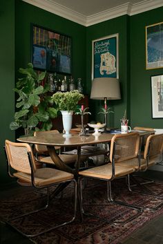 a dining room with green walls and wooden table surrounded by chairs, potted plants and pictures on the wall